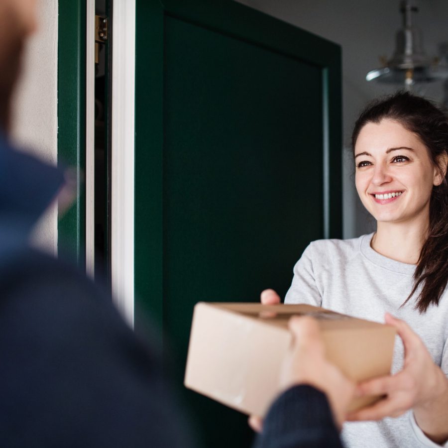 Woman receiving parcel from unrecognizable delivery man at the door - courier service concept.